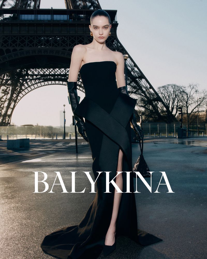 Fashion shot of a woman in a black gown posing in front of the Eiffel Tower in Paris. The image features elegant attire and Parisian scenery.