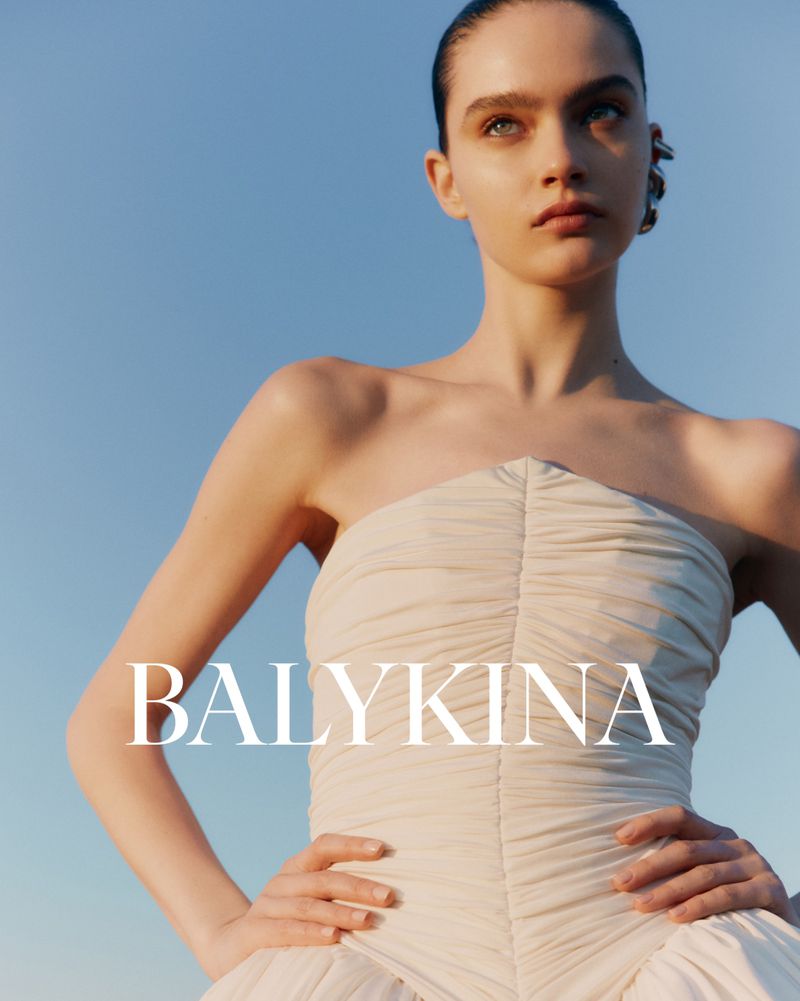 A fashionable woman in a dress poses against a clear sky in a beauty or fashion editorial advertisement showcasing a dress design.