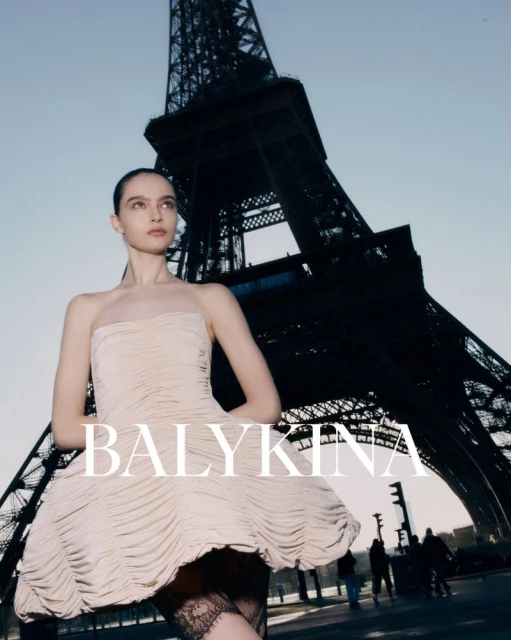 Fashion shot in Paris featuring a woman in a dress posing in front of the Eiffel Tower on a sunny day with pedestrians walking.