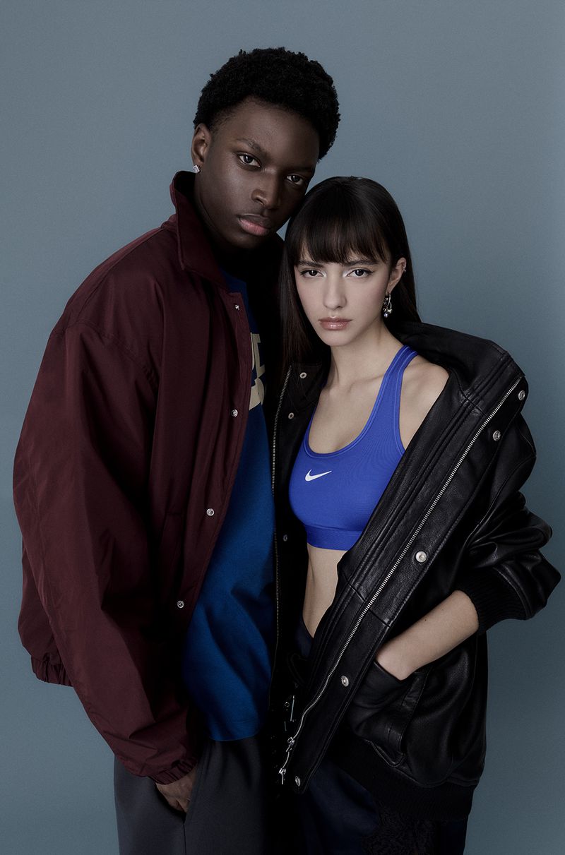 Portrait of a young mixed ethnicity couple in studio, wearing athletic tops and jackets, with a neutral facial expression against grey background.