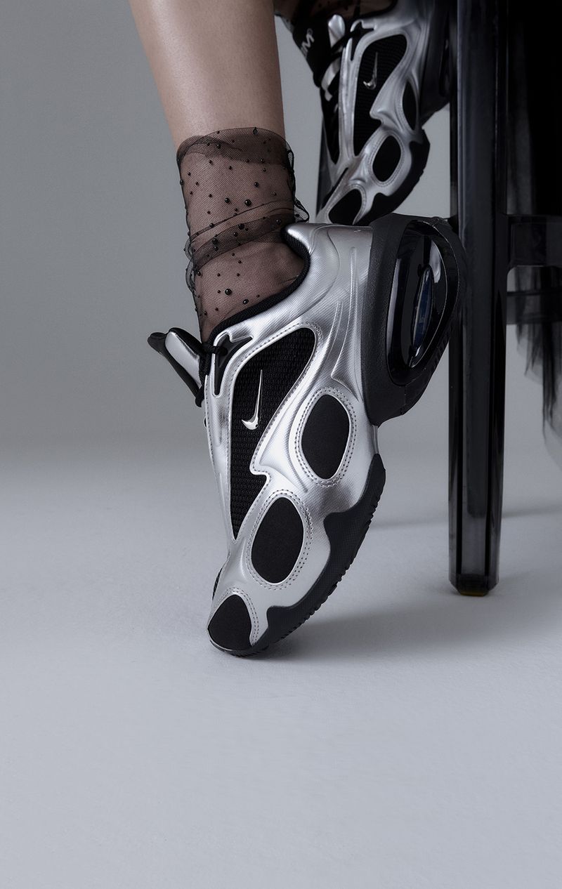 A pair of silver Nike sneakers are captured in a studio shot, displayed on a gray surface with a sleek black chair in the background.