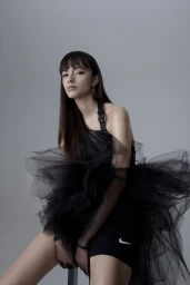 Woman with long dark hair wearing a black tulle dress against a plain grey background