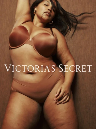 Woman in lingerie for Victoria's Secret, laying on side, brown skin, brown strapless bra and underwear, against a brown background.