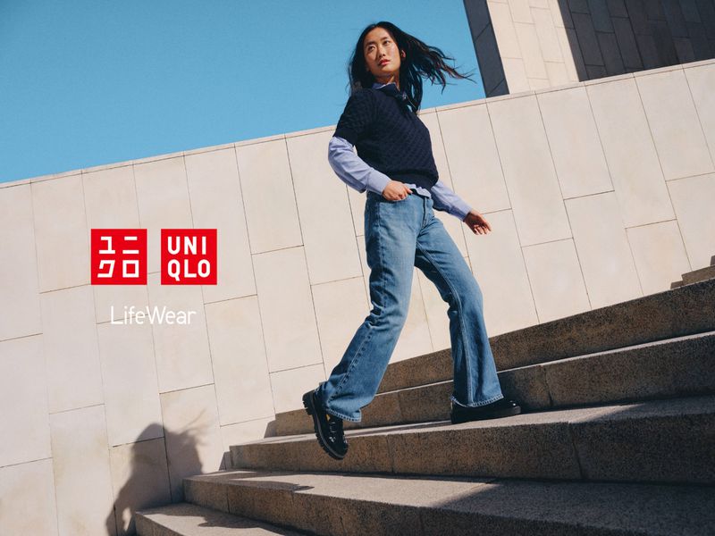 A young woman in jeans and a sweater walks down stone steps in an outdoor urban setting, with the UNIQLO LifeWear logo visible.