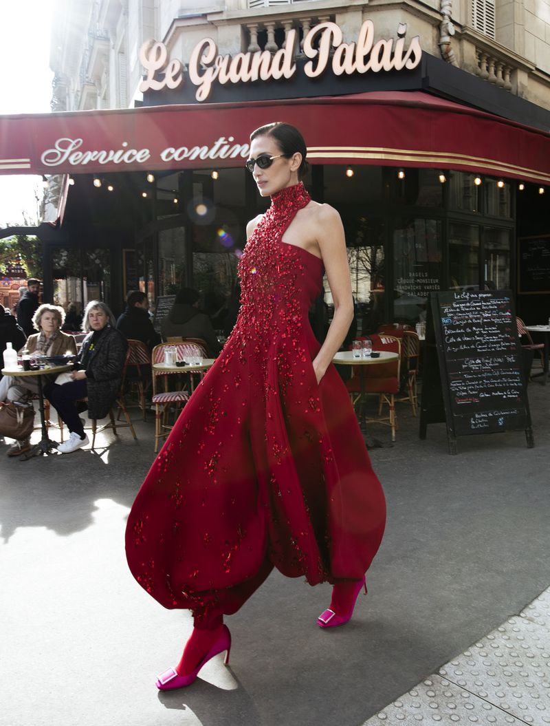 Fashionable woman in a red sequined dress walks in front of Le Grand Palais cafe on a sunny day in Paris. Couture fashion editorial.