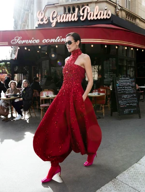Model Nieves Alvarez in a red embellished halter gown walking past a Paris café for Elle Spain.