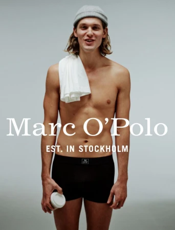 Young man in underwear and a beanie poses in a studio, holding a coffee cup, with the Marc O'Polo logo prominently displayed.