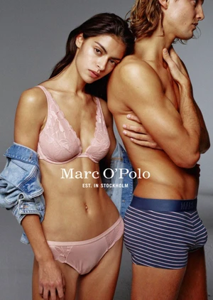 A woman in a pink lace bra and underwear leaning her head on the shoulder of a shirtless man wearing striped boxer briefs.
