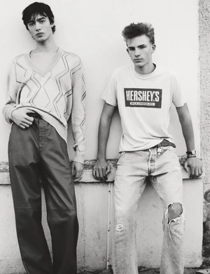 Two young male models leaning against a plain wall for the Young and in Paris project by HERO Magazine.