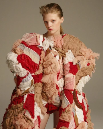 Fashion model in a photo studio. She is wearing an avant-garde patchwork dress made of red, beige and white textured fabrics. 