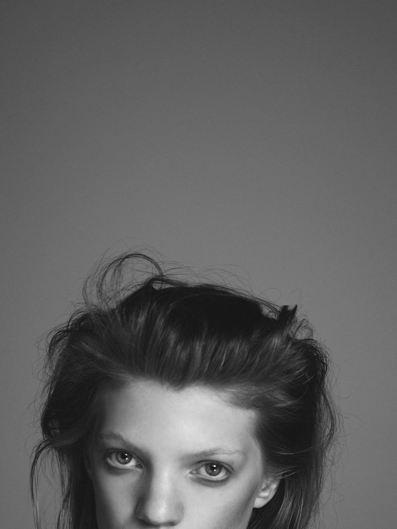 Monochrome portrait of a fair-skinned adult woman with messy dark hair, captured in a close-up shot against a plain grey backdrop.