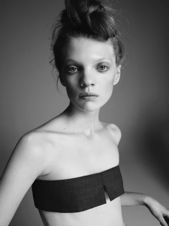 Monochrome portrait of a young woman with a top-knot hairstyle and a dark strapless top against a neutral grey backdrop.
