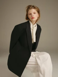 Model with red hair wearing a black blazer and white blouse against a neutral grey studio background