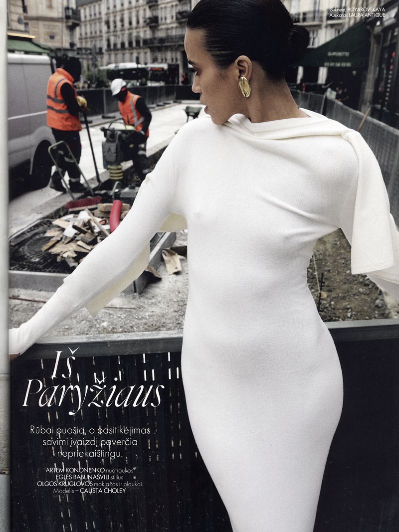Fashion editorial shot of a woman in a white dress standing in front of a construction site in an urban environment.