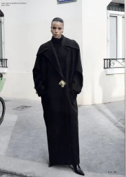 Model standing on a paved street wearing a long black coat and turtleneck, photographed for Elle Lithuania.