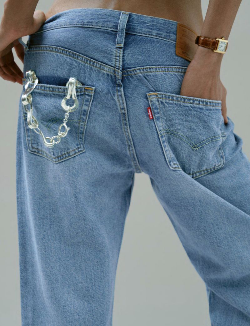 Woman wearing light blue jeans and silver chain. One hand is in the pocket and a brown watch is seen on the wrist.