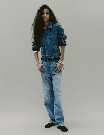 Model in denim jacket and jeans standing against a plain neutral background
