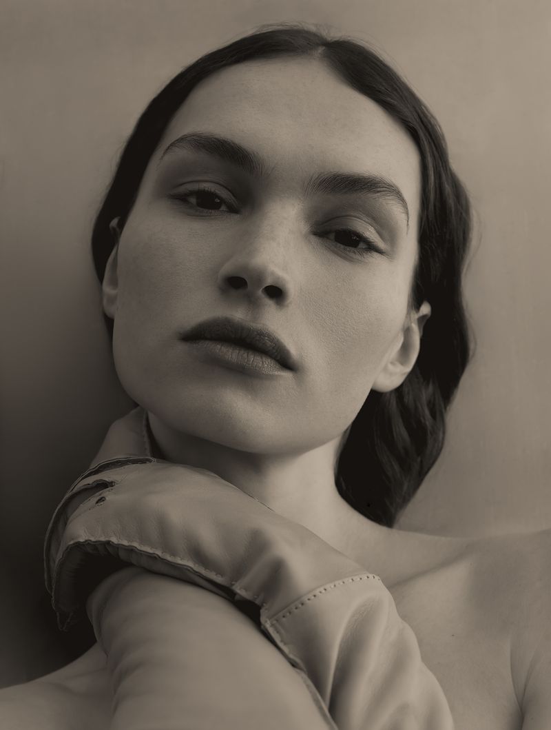 Monochrome portrait of a woman with bare shoulders and dark hair, wearing a satin glove, captured in a soft, diffused light.