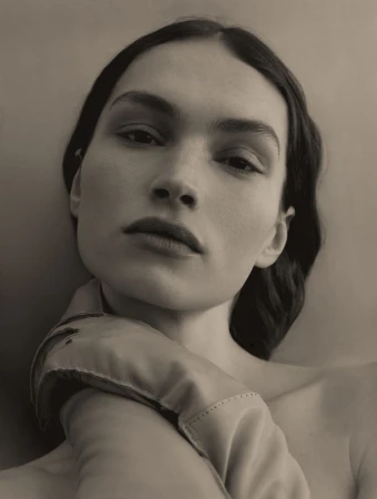 Monochrome portrait of a woman with bare shoulders and dark hair, wearing a satin glove, captured in a soft, diffused light.
