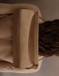 Close-up of a tan leather handbag worn horizontally across a model's bare back with dark wavy hair