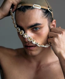 Close-up portrait of model Pablo Fernandez holding a rhinestone chain across his face while wearing a wig cap.