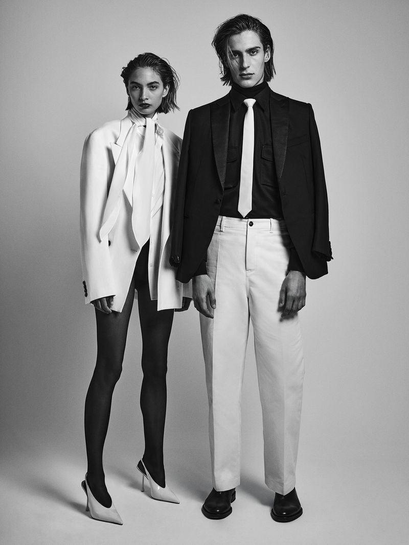 Black and white studio shot of a stylish male and female fashion models posing in blazers, dress pants, and dress shoes.