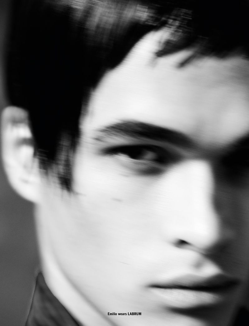 Close-up black and white portrait of a young adult male with short dark hair looking forward. The image has slight motion blur.