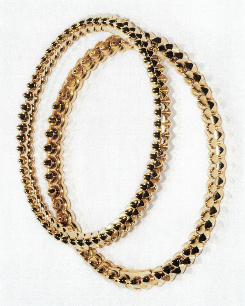 Close-up studio shot of two golden, rigid necklaces with repeating geometric pattern, showcasing jewelry design and precious metal aesthetic.