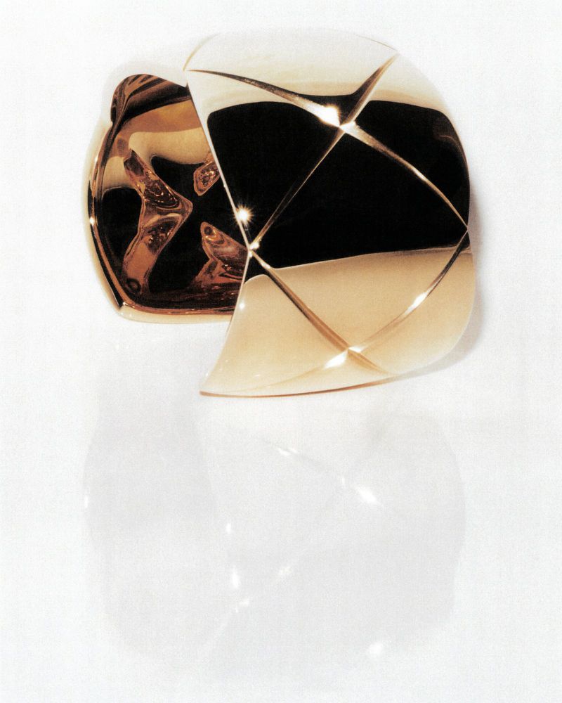 Elevated, close-up studio shot of a geometric gold cuff bracelet with a glossy finish, set against a bright white seamless background.