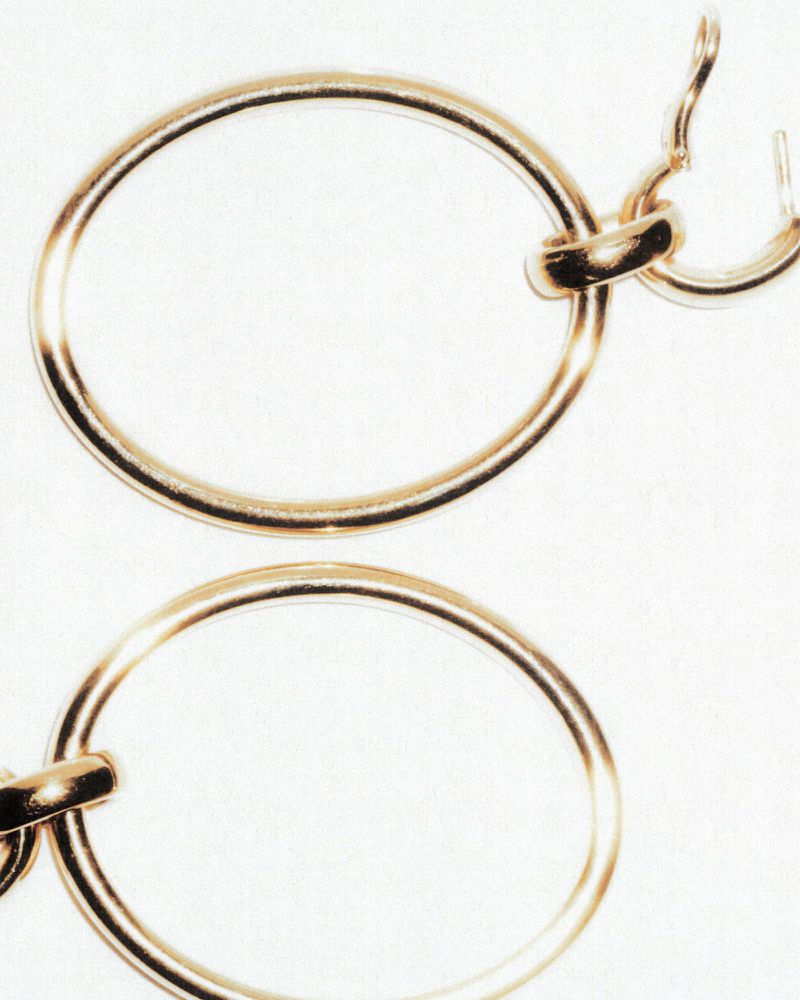 Macro shot of gold hoop earrings. The pair of earrings are connected, hanging vertically against a plain white backdrop.