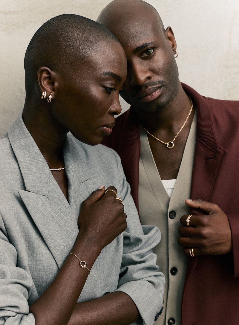 An elegant studio portrait of a fashionable African-descent couple wearing jewelry and stylish blazers against a neutral backdrop.