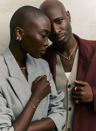 An elegant studio portrait of a fashionable African-descent couple wearing jewelry and stylish blazers against a neutral backdrop.