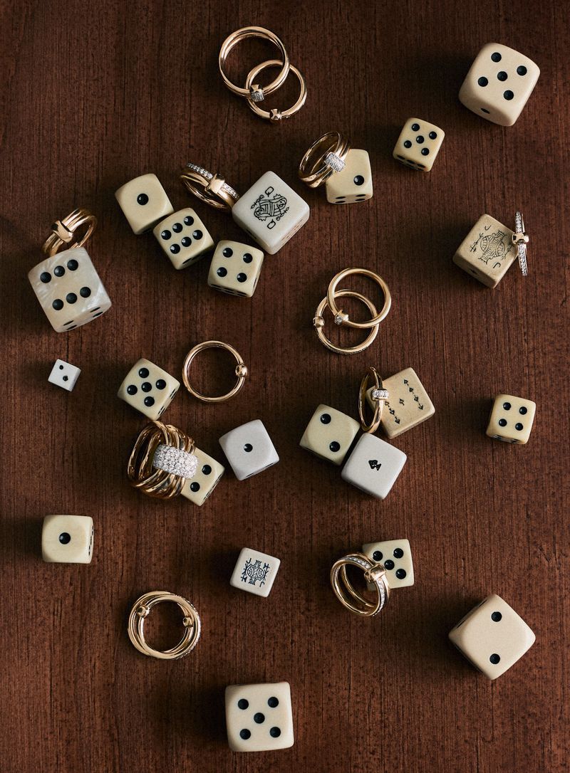 Overhead shot displaying an arrangement of rings and dice on a wood surface, creating a blend of luxury jewelry and gaming elements.