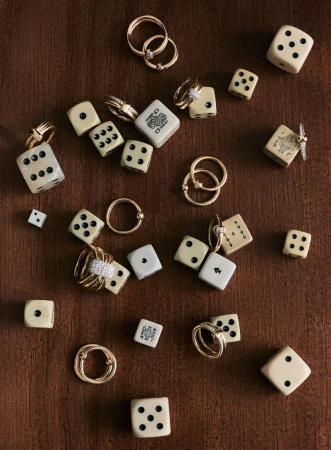 Overhead shot displaying an arrangement of rings and dice on a wood surface, creating a blend of luxury jewelry and gaming elements.