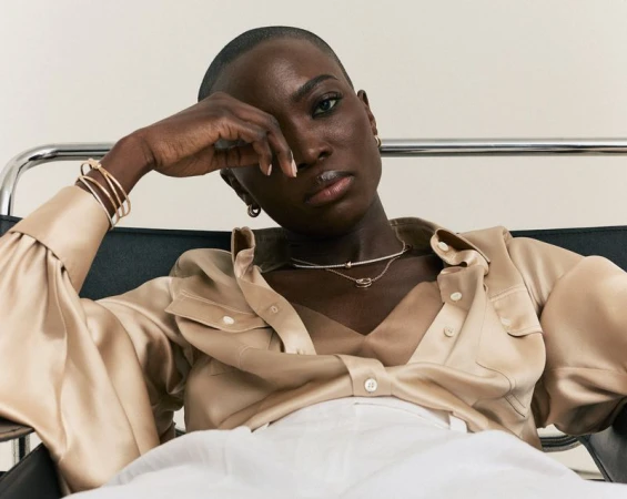 Portrait of a stylish Black woman with short hair in a champagne-colored blouse and white pants, shot in a studio setting.