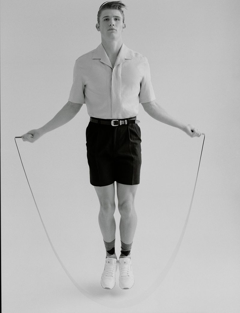 Young man in retro athletic wear skipping rope in a studio. Black and white portrait of a man exercising in white sneakers and dark shorts.