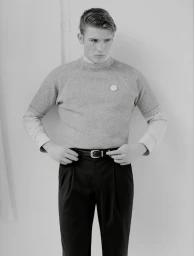 Monochrome portrait of a male model wearing a short-sleeve knit top, collared shirt, and dark trousers against a plain studio background.
