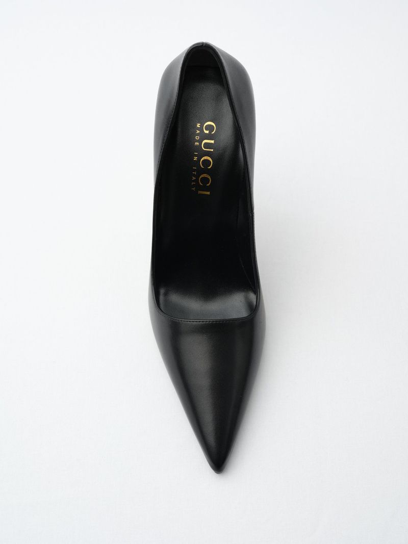 Black leather Gucci stiletto heel on white. The designer shoe is displayed from above showing pointed toe, heel, and gold logo.