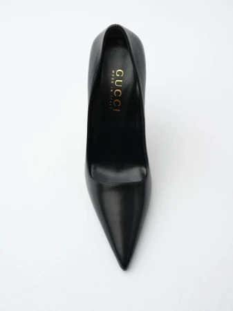 Black leather Gucci stiletto heel on white. The designer shoe is displayed from above showing pointed toe, heel, and gold logo.