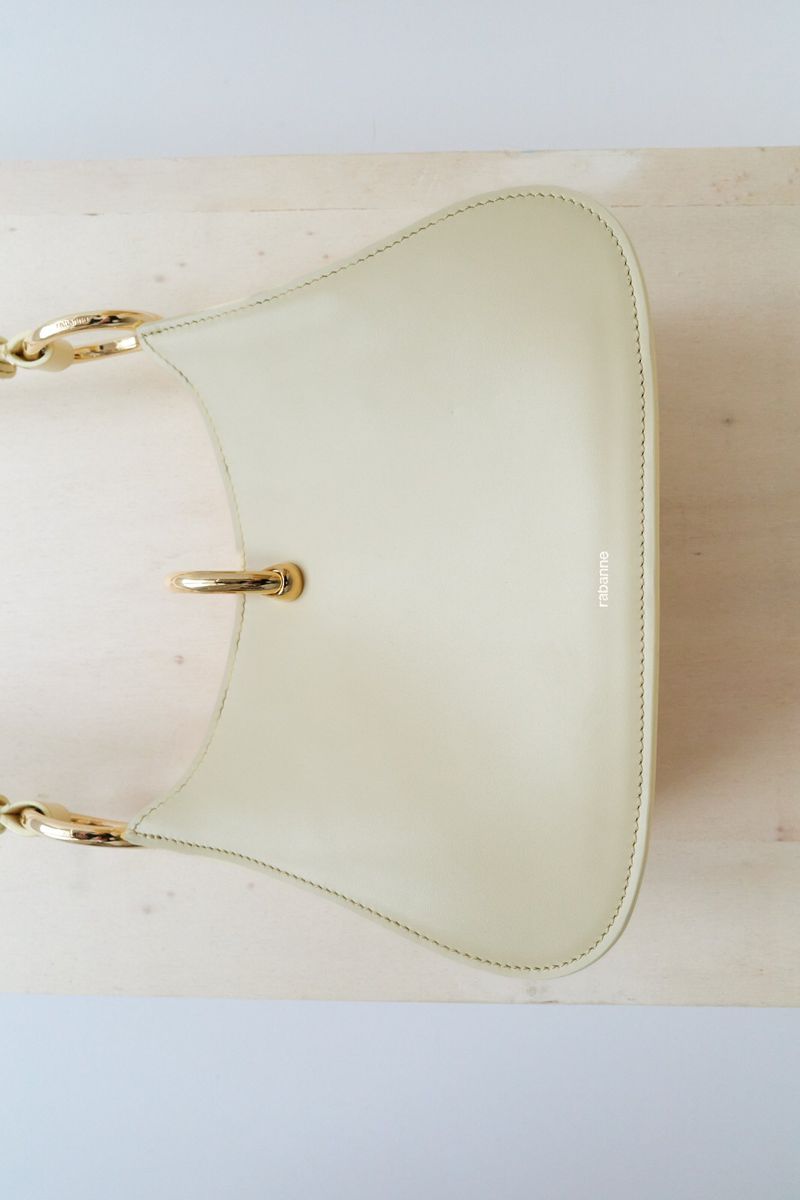 Fashionable yellow leather purse with gold chain detail on a marble surface, luxury handbag with gold hardware, studio shot.