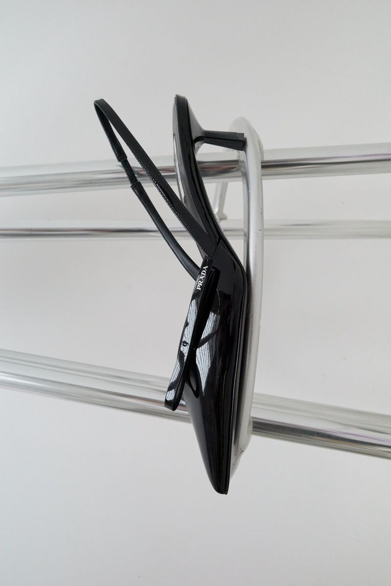 Elegant black Prada heeled sandal with ankle strap displayed on a polished chrome rack against a clean white backdrop.