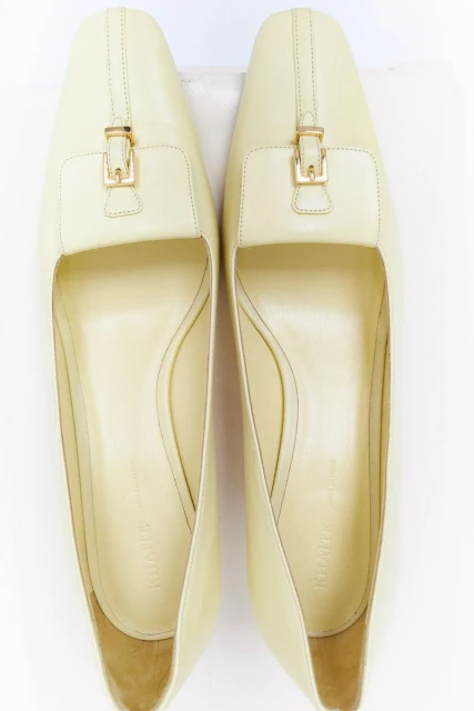 Overhead shot of pair of cream-colored leather heeled shoes with gold buckle detail against a white background. Stylish women's footwear.