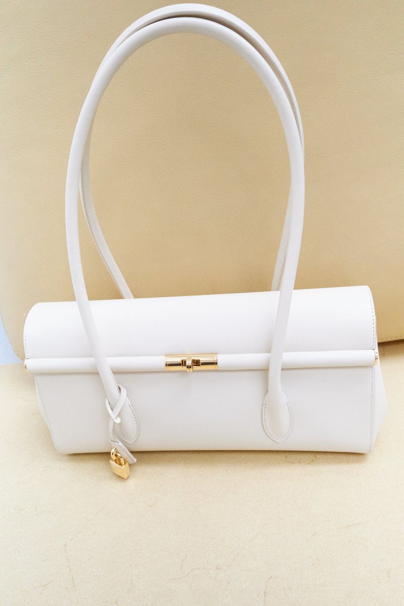 Elegant white leather handbag with gold accents, featuring a structured design and curved handles, set against a neutral background.