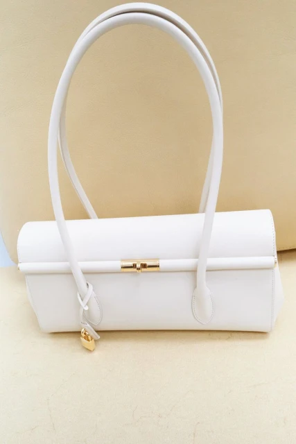 Elegant white leather handbag with gold accents, featuring a structured design and curved handles, set against a neutral background.