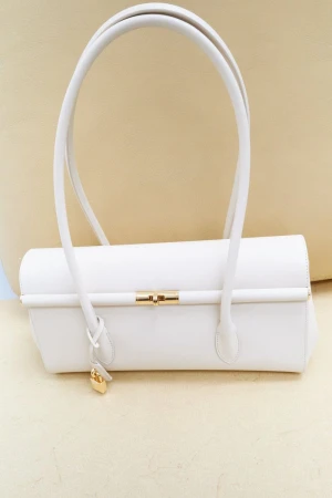 Elegant white leather handbag with gold accents, featuring a structured design and curved handles, set against a neutral background.