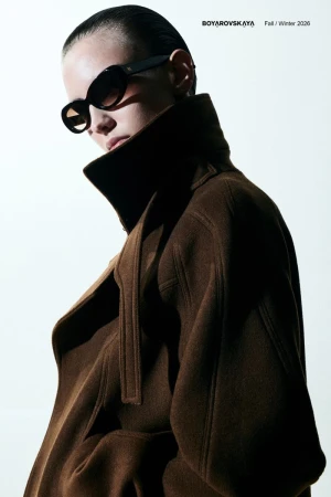 Model in dark sunglasses wearing a brown wool coat against a bright white background