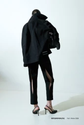 Model wearing a black jacket and slit trousers carrying a black handbag against a white background for Boyarovskaya FW26.