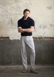 Full-length portrait of a male model wearing a dark sweater with a sweater tied over his shoulders and light grey trousers.
