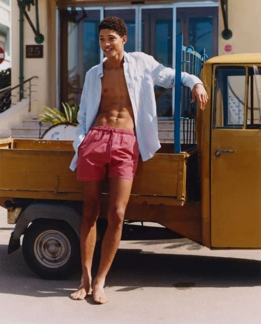Young man with open shirt, posing next to yellow truck. Summer outdoor fashion shot of male model near vehicle, bathed in sunlight.