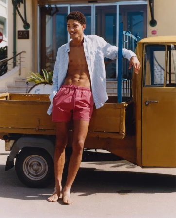 Young man with open shirt, posing next to yellow truck. Summer outdoor fashion shot of male model near vehicle, bathed in sunlight.